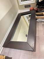 Full view of large dark brown wood framed mirror lying flat