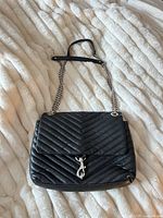 Full view of black quilted leather bag with chain strap displayed on fabric