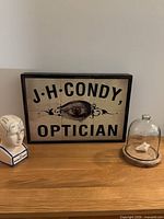 Optician tile sign centered, phrenology bust left, cloche right