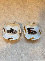 Both porcelain ashtrays side by side showing automobile illustrations and gold trim