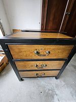 Front view showing three drawers, floral motifs, metal bail pulls, black frame.