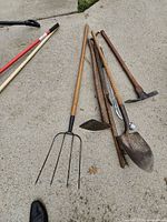 Group of yard tools on concrete showing pitchfork, shovel, hoes