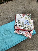 Folded teal quilt and floral shams on ground