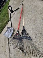 Snow shovel and two leaf rakes on driveway