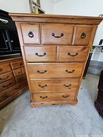 Front view of tall honey-brown dresser showing all drawers and hardware