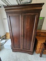 Front view of closed media armoire showing paneled double doors, crown molding, plinth base