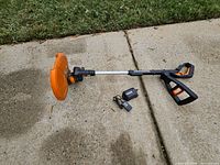 Full view of Worx cordless string trimmer/edger lying on pavement with battery and charger