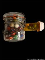 Glass jar filled with marbles with pill bottle of additional marbles attached