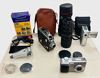 All items laid out on table: cameras, camcorder, lens, cases, accessories