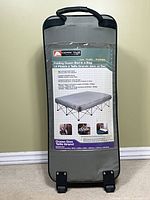 Front of wheeled carry case displaying product label for Ozark Trail folding queen bed
