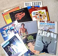 Group shot of first stack of records showing Fame, Top Gun, Rocky III, Platoon, Bill Cosby and others
