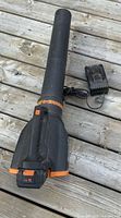 Full view of leaf blower with battery attached and charger beside it on wooden deck