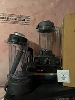Front view of Vitamix blender base with two pitchers, tamper, extra lid and box