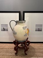 Front view of ceramic jug on wooden stand before framed pictures