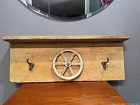 Front view of wooden coat rack showing pulley wheel and two metal hooks