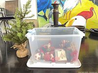 Tabletop tree beside clear bin filled with ornaments, cards, ribbon