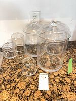 Group of five clear glass canisters with lids on countertop