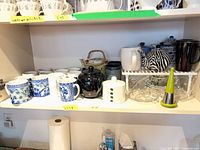 Shelf showing mugs, teapots, sugar bowl, glass teacups and juicer