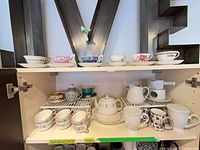 Cabinet shelf showing full assortment of Minton set and assorted branded teacups
