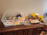 Overview of lot on wooden cabinet showing bin of buttons, cups, game and tins