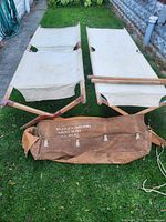 Two assembled wooden cots and canvas bag on grass