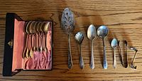 All 14 pieces laid out including cased spoons, server, spoons, tongs, ladle