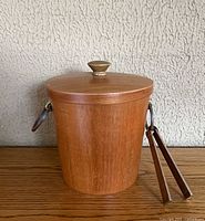 teak ice bucket with lid on, tongs hanging from handle
