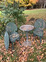 Two chairs, birdbath and round tabletop leaning against chair