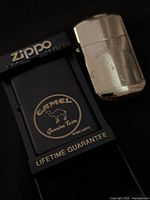 Black Camel Zippo lighter in display next to brass lighter