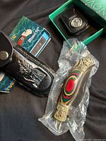 Pocket knife in plastic wrap beside black leather sheath and original small box