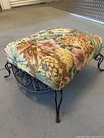 Full view of footstool showing floral tapestry top and metal scroll legs