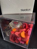 Watch in clear acrylic cube with outer Swatch sleeve visible