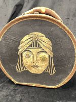 Front of round black hat box showing gold face graphic and wear