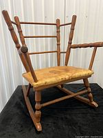 Front angled view of small wooden child rocking chair showing spindle back and rocker base