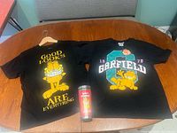 Both Garfield t-shirts and travel mug displayed on table