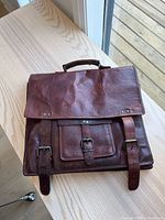 Front view of brown leather briefcase with flap, buckles, front pocket