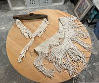 Two macrame wall hangings laid out on table: wide fringe piece and driftwood-mounted V-shape