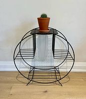 Front view of round black metal wire plant stand showing four shelves