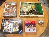 All five items—three boxed 1000-piece puzzles, one board game, one round tin wooden puzzle—group shot