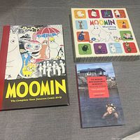 Front view of all three items: hardcover comic compilation, matching game box, paperback book