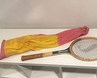 Rolled pink/yellow tent sleeve beside wooden Spalding racquet