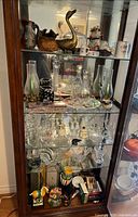 Full cabinet view showing quantity and variety of glassware, ceramics, brass figurine and packaged items