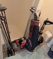 Full view of golf bag, pull cart, box of golf balls and clubs