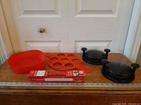 All items laid out: red silicone baking dish, egg ring, boxed baking sheet, two black chicken shredders