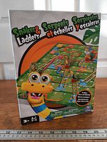 Front of sealed Snakes and Ladders box showing artwork, age 3+, 2-4 players icons and Spin Master logo