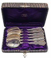Open fitted case displaying six ornate sterling spoons in purple lining