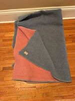 Full view of folded reversible wool throw showing blue-gray top and pink underside