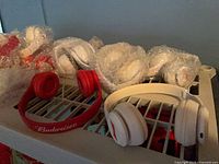 Shelf with unwrapped red and white Budweiser headphones plus multiple bubble-wrapped units