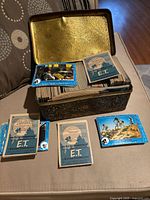 Tin open displaying stack of E.T. trading cards with several cards laid out
