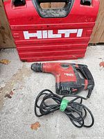 Rotary hammer with power cord beside red Hilti case